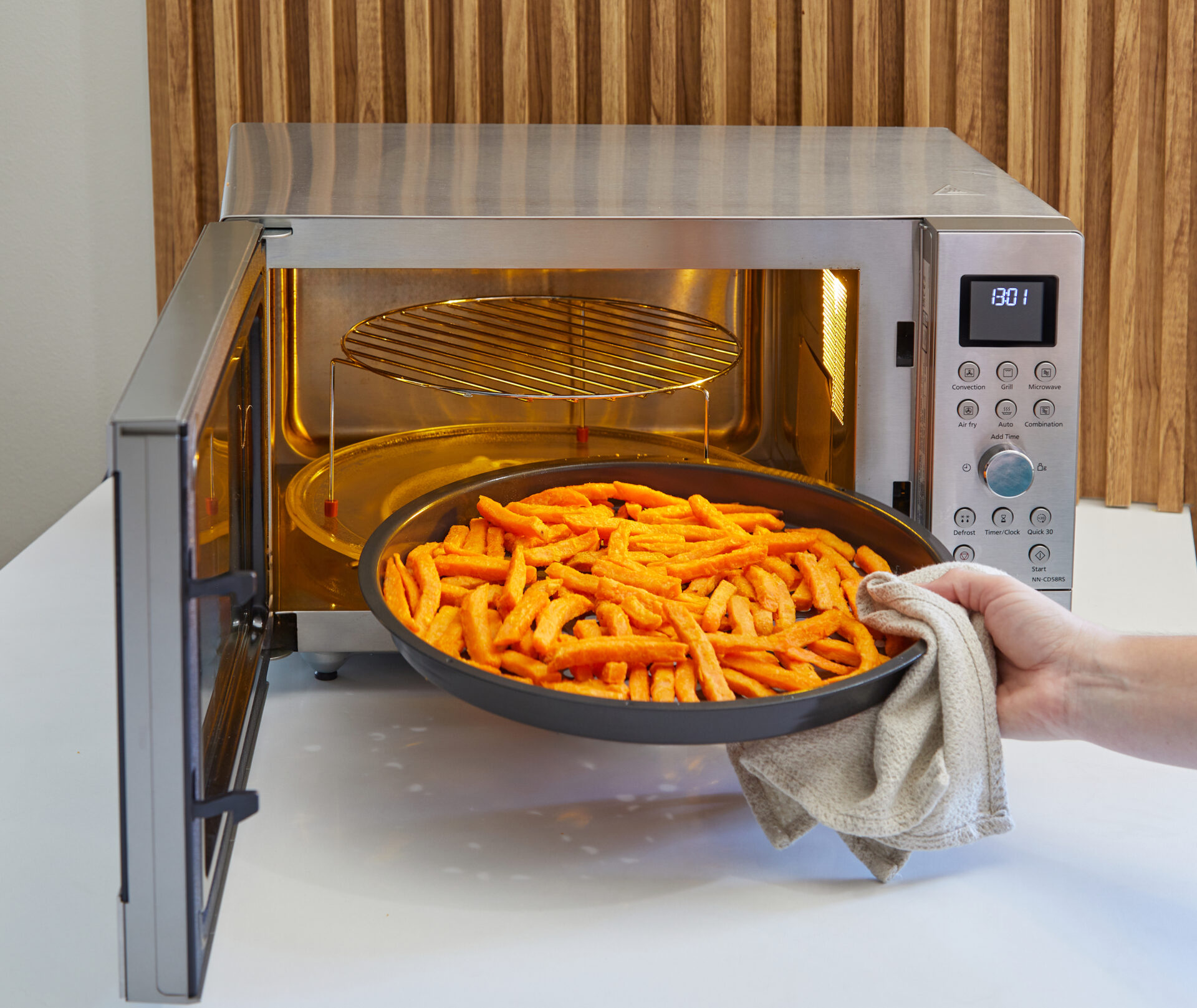 O tavă plină cu cartofi prăjiți tăiați este introdusă în cuptorul cu microunde mixt Panasonic Slim Line, cu grătarul vizibil la nivelul superior.