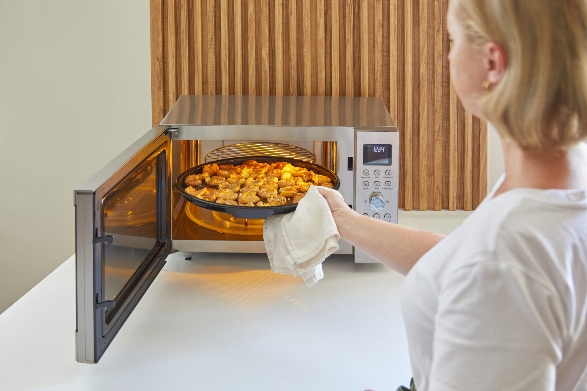 Se scoate o tavă cu mâncare din cuptorul cu microunde mixt Panasonic Slim Line, iar mâncarea se așează pe grătarul din interiorul aparatului.